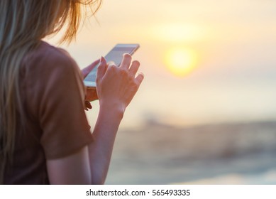 woman texting on smart phone on the beach during sunset - Powered by Shutterstock