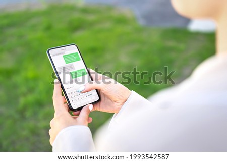 Woman texting with phone outdoors. Text message with smartphone. Digital sms and instant messaging chat. Person using cellphone in park outside in summer. Conversation with boyfriend or friend.