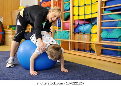 Woman as a therapist at physiotherapy with medicine ball with child in gym
