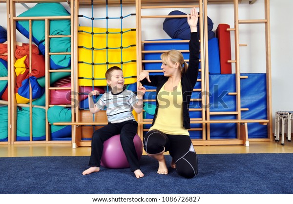 Woman as a therapist at physiotherapy with medicine\
ball with child in gym