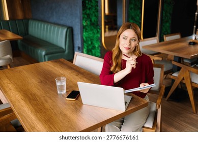 Woman thinking and writing notes while remote working in a modern cafe
