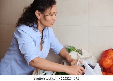 A woman thoughtfully organizes her groceries in the kitchen. Fresh fruits and vegetables are displayed, reflecting a focus on healthy eating and home management. - Powered by Shutterstock