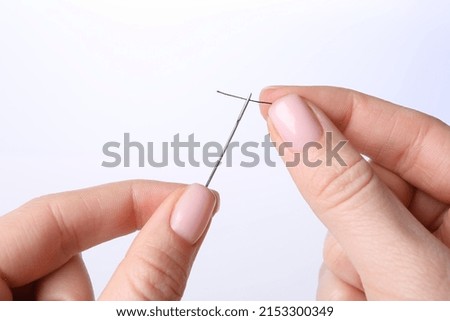 Woman threading sewing needle on white background, closeup