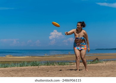 Woman throwing a frisbee on a sandy beach on a sunny day. body positive - Powered by Shutterstock