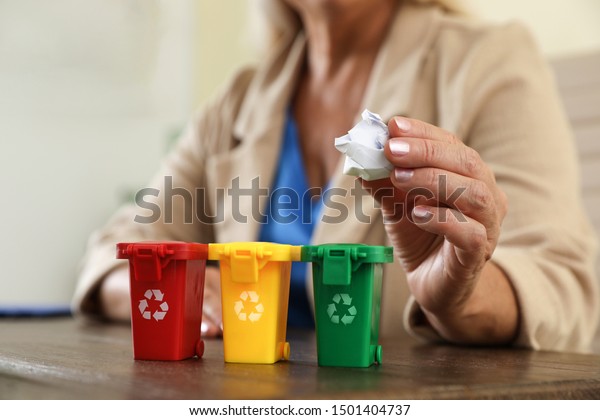 Woman throwing paper into mini recycling bin at\
office, closeup