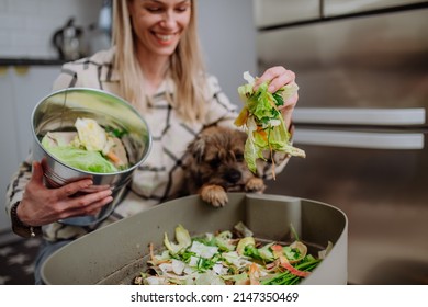 Woman throwing vegetable cuttings in a compost bucket in kitchen and feeding dog. - Powered by Shutterstock