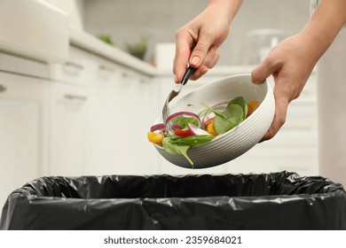 Woman throwing vegetable salad into bin indoors, closeup