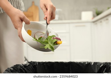 Woman throwing vegetable salad into bin indoors, closeup - Powered by Shutterstock