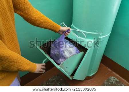 A woman throws a bag of garbage into a garbage chute at the entrance of an apartment building in Russia