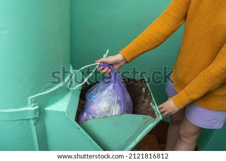A woman throws a bag of garbage into a garbage chute at the entrance of an apartment building in Russia. Close up