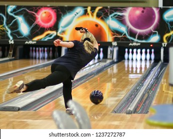 A woman throws a bowling ball on the track in order to knock down the pins.