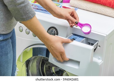 Woman throws laundry detergent into the washing machine close-up.