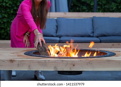 woman throws logs on fire pit in the garden on a summer day close-up