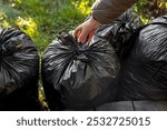 Woman throws out garbage in black garbage bags. Garbage collection on street or in garden