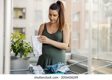 The Woman Tidies Up The Messy House, The Mother Stacks The Baby Clothes. A Woman With A Tail Neatly Prepared Dry And Clean Laundry During The Day On The Terrace. House Cleaning, Household Chores