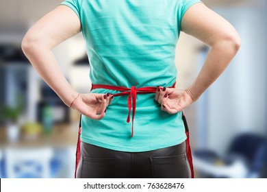 Woman tie a back knot of red apron getting ready to clean or cook. Close-up concept. - Powered by Shutterstock