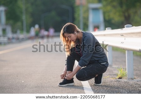 woman tie shoelaces on road. Cheerful runner sitting on floor on city streets with mobile and earphones wearing sport shoes. Active asian woman tying shoe lace before running.