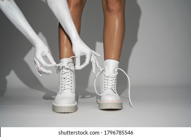 Woman Ties The Laces On White Shoes On A Light Background In The Studio. Close-up Fashion Footwear New Collection Autumn Winter. Fashion Shooting                            