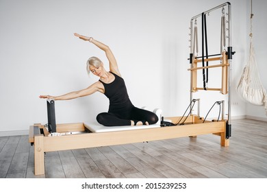 woman in tight sportswear doing pilates on a reformer in a white gym