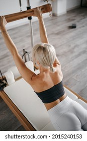 woman in tight sportswear doing pilates on a reformer in a white gym