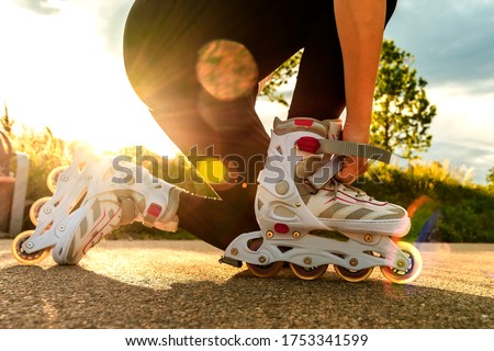 A woman tightens roller skates on the path. Woman's legs with roller blades at sunny day.