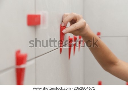 Woman tiling bathroom walls. Flat wall plastic tile leveling system. Process of installation of tiles in the bathroom. DIY home improvement.