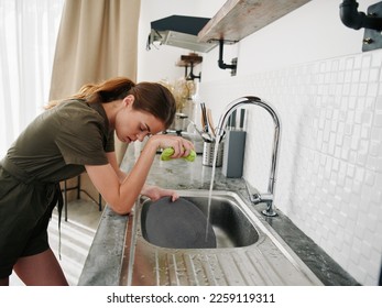 Woman tired and angry hands without gloves washes dishes with a dishwashing sponge, household chores, no dishwasher, high water consumption. Stylish kitchen design - Shutterstock ID 2259119311