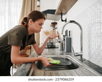 Woman tired and angry hands without gloves washes dishes with a dishwashing sponge with bubbles, household chores, no dishwasher, high water consumption. Stylish kitchen design - Powered by Shutterstock