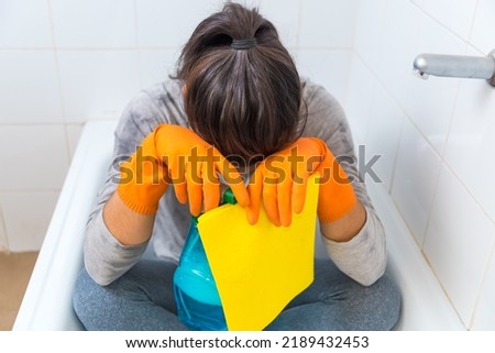 woman tired of cleaning the bathroom, frustrated, sitting in the bathtub with cleaning supplies in her hand, crestfallen
