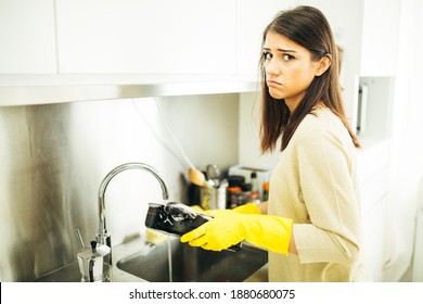 Woman Tired Of Hand Washing And Cleaning Chores.Housewife Woman Washing Dishes In Kitchen. Washing Dishes Manually, Wearing Yellow Cleaning Rubber Gloves. Making A Sad Face. Disgusted And Annoyed Girl