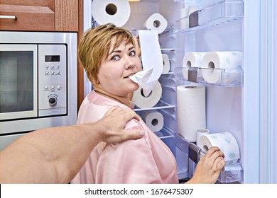 Woman with toilet paper by the refrigerator was caught her husband during nightly meal. Prank of over-buying toilet paper during coronavirus