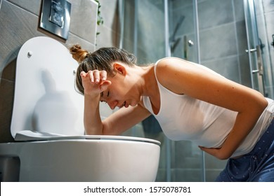Woman in toilet - pregnant, drunk or illness concept. Young dark-haired woman vomiting in toilet. Woman getting sick and vomiting over a toilet bowl kneeling down with her arms resting on the seat