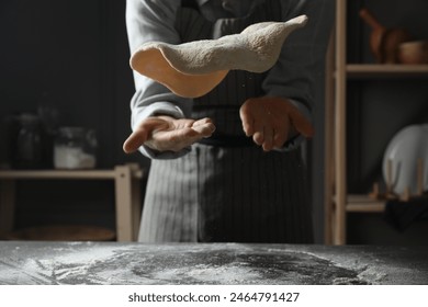 Woman tossing pizza dough at table in kitchen, closeup