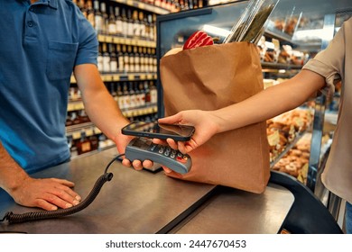 A woman touches a smartphone to a terminal while paying for food in a grocery store. Large purchase of food in the supermarket. - Powered by Shutterstock