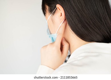 Woman Touching Backs Of Her Ears And Suffering From Ear Pain That Caused By Wearing Medical Face Mask, Result In Skin Irritation Or Contact Dermatitis.