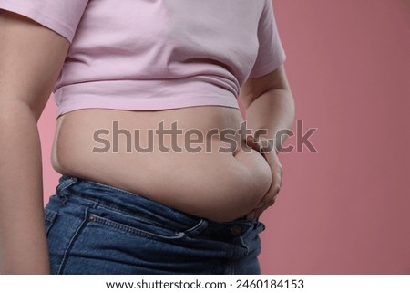 Woman touching belly fat on pink background, closeup. Overweight problem