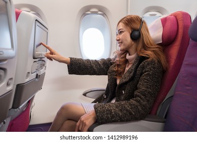 Woman Touching LCD Entertainment Screen On The Airplane In Flight Time.