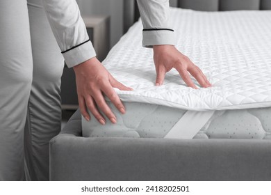 Woman touching new soft mattress on grey bed in bedroom, closeup