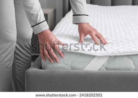 Woman touching new soft mattress on grey bed in bedroom, closeup