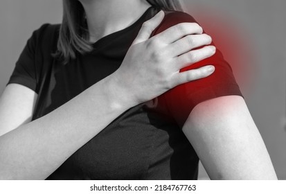 Woman touching painful shoulder with red point. Arm ache, swelling. Overuse, rotator cuff tendons injury, dislocation consequences. Health problems concept. Black and white. High quality photo
