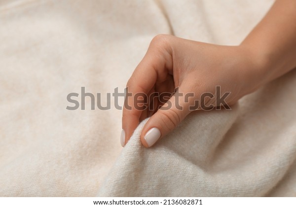 Woman\
touching soft beige knitted fabric,\
closeup