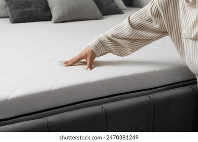 Woman touching soft orthopedic mattress on bed at home, closeup