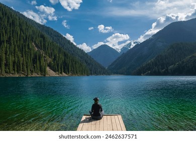 A woman, a tourist, admires the view from a wooden pier on a mountain lake with turquoise clear water. Lake Kolsai or Kulsay in the mountain range of Kazakhstan. - Powered by Shutterstock