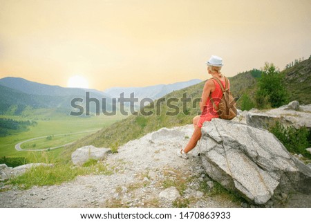 Woman Tourist With A Backpack Sitting, Resting On A Mountain Top On A Rock On The Journey. Woman hiker sitting on rock on top of hill while looking at sunset