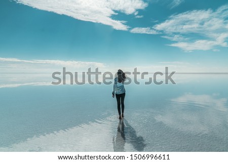 Woman tourist & beautiful mirror reflection on blue sky and cloud on Bolivia's Salt Flats. Shot in Salar de Uyuni salt flat. Water reflection of clouds and empty space. Holiday, vacation travel scene 