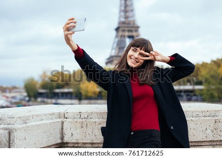 Woman tourist at Eiffel Tower smiling and making travel selfie. Beautiful European girl enjoying vacation in Paris, France