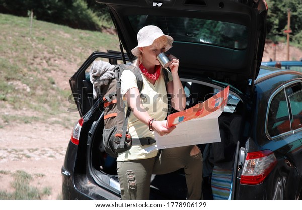 Woman\
tourist looking at map,drinking coffee in car\
trunk