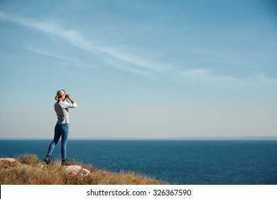Woman tourist looking through binoculars at distant sea, enjoying landscape
