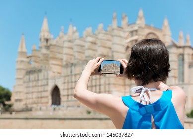 Woman tourist in Mallorca taking photographs of landmark buildings while enjoying the adventure of a a summer vacation in Europe, view from behind