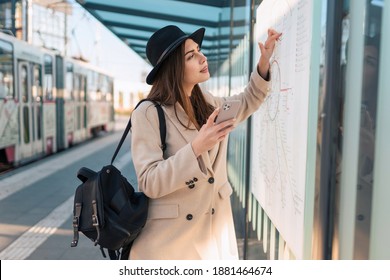 Woman tourist with phone in hand at bus stop looking on map of public transport routes